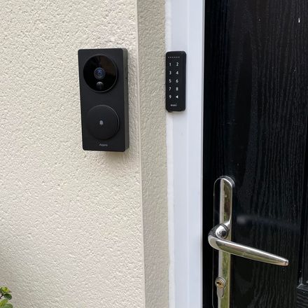 Interphone vidéo Aqara et clavier à code fixés au mur, à l'entrée d'un logement — la porte garde sa poignée mécanique d'origine.
