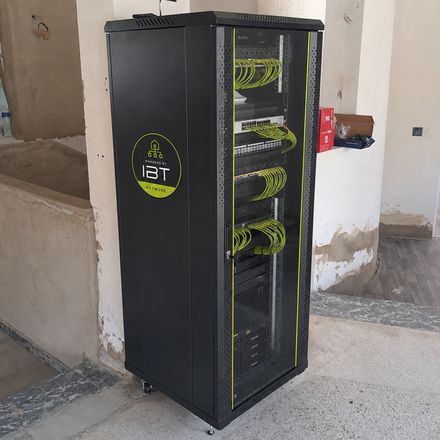 Baie de brassage IBT installée sur un chantier en cours de finition, porte vitrée ouverte sur les bandeaux de brassage, les commutateurs et les cordons verts peignés niveau par niveau.